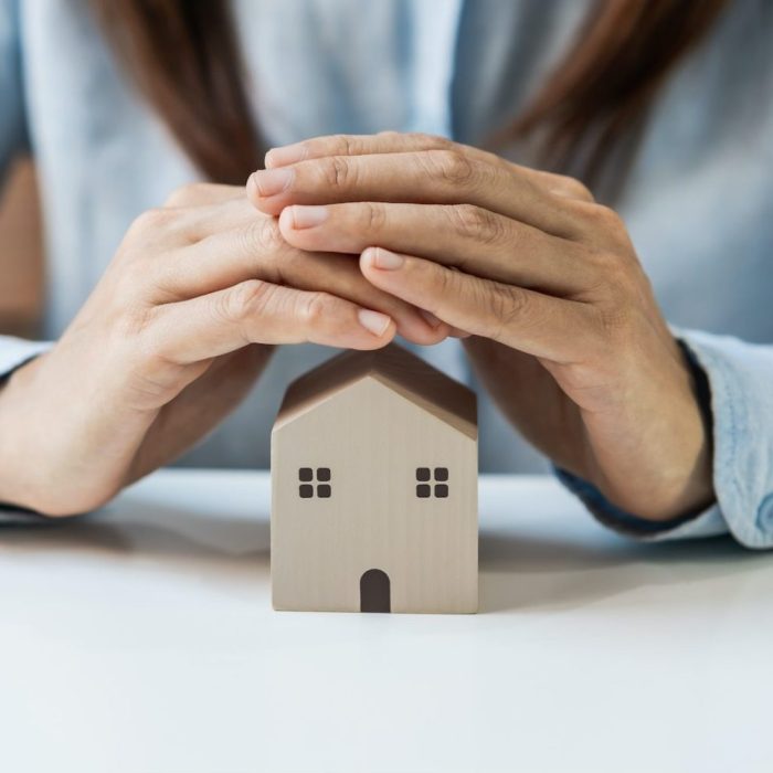 Young woman hands protecting miniature house, Home insurance concept